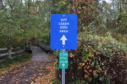 Off-leash dog area directional signage – hard surface to wooden bridge with railings Off-leash dog area directional signage – hard surface to wooden bridge with railings